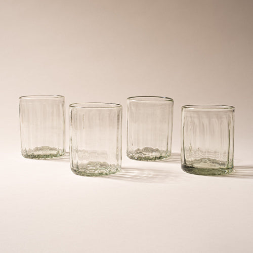 Four taller clear textured glass tumblers with vertical ridges against a neutral background.