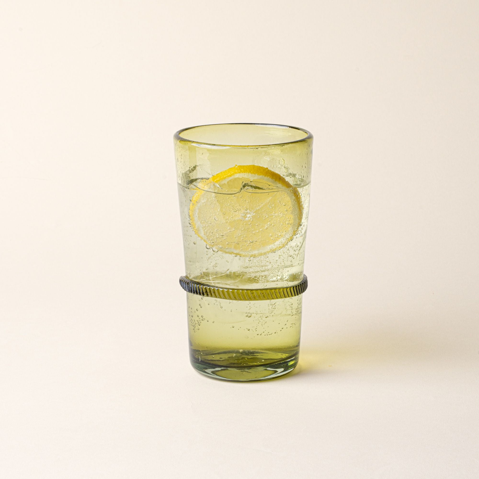 An olive tall recycled glass tumblers with a ridged band detail, filled with water and a lemon slice.
