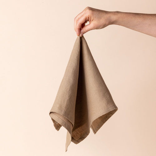 Hand holding a linen napkin in an soft warm brown color from the center