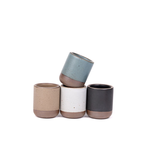 A set of 4 small, short ceramic mug cups in a blue-grey, graphite black, cool white, and warm pale brown colors featuring iron speckles and unglazed rim