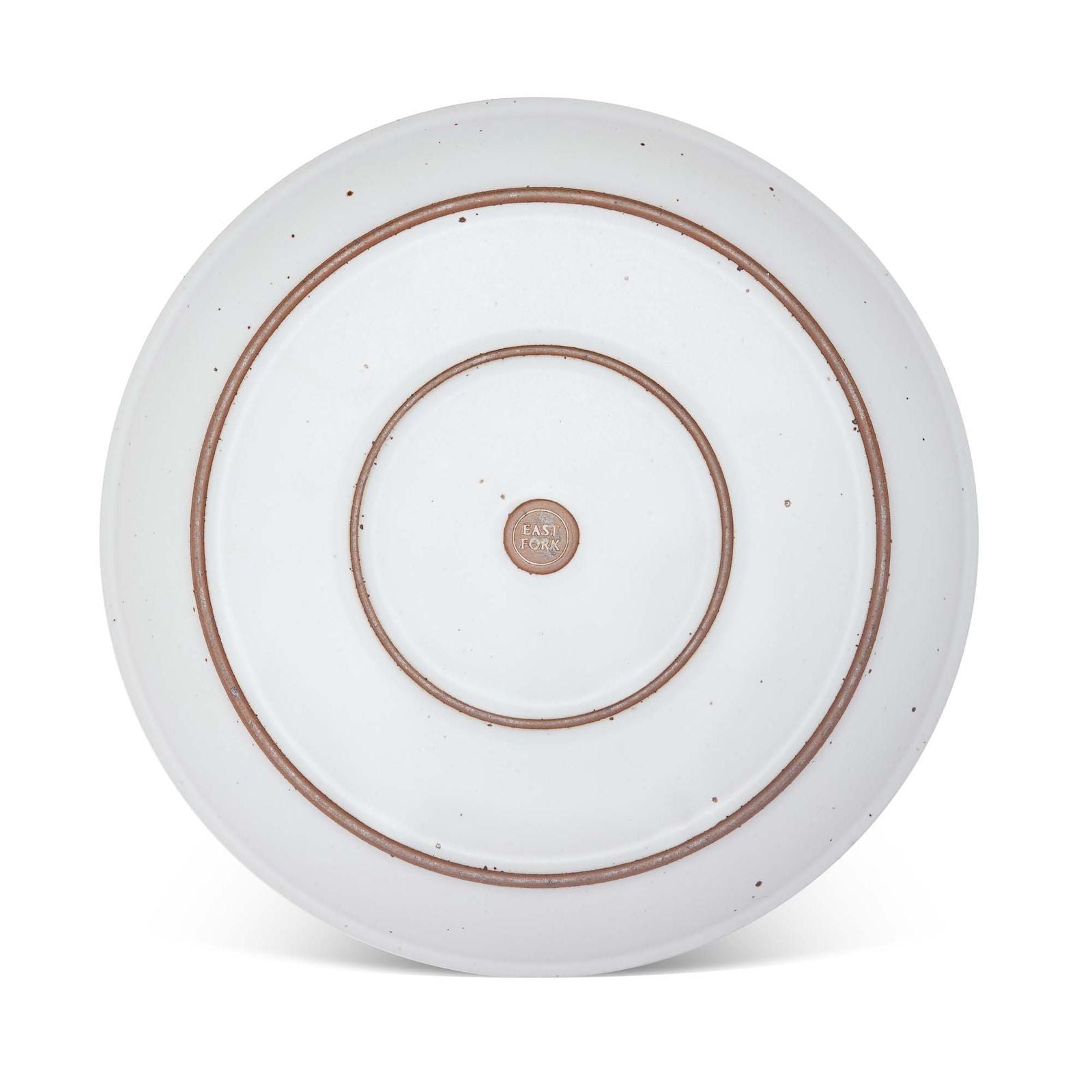 The bottom of a large ceramic platter in a cool white color featuring iron speckles and an unglazed rim.