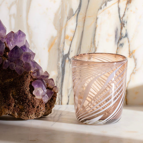 Smoky glass tumbler with white swirl pattern beside an amethyst crystal cluster on marble.