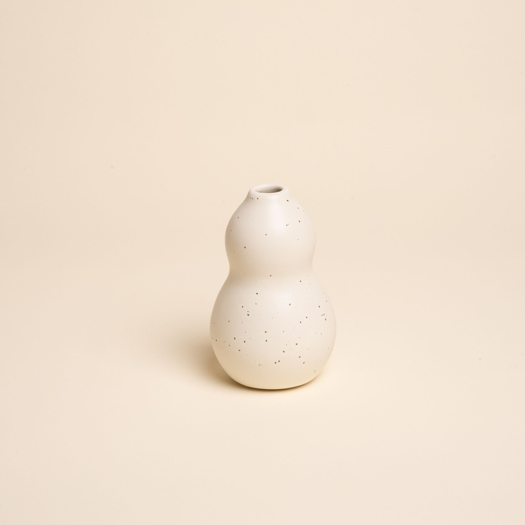 Small off-white ceramic vase with a curvy shape and subtle speckles, set against a soft beige background.