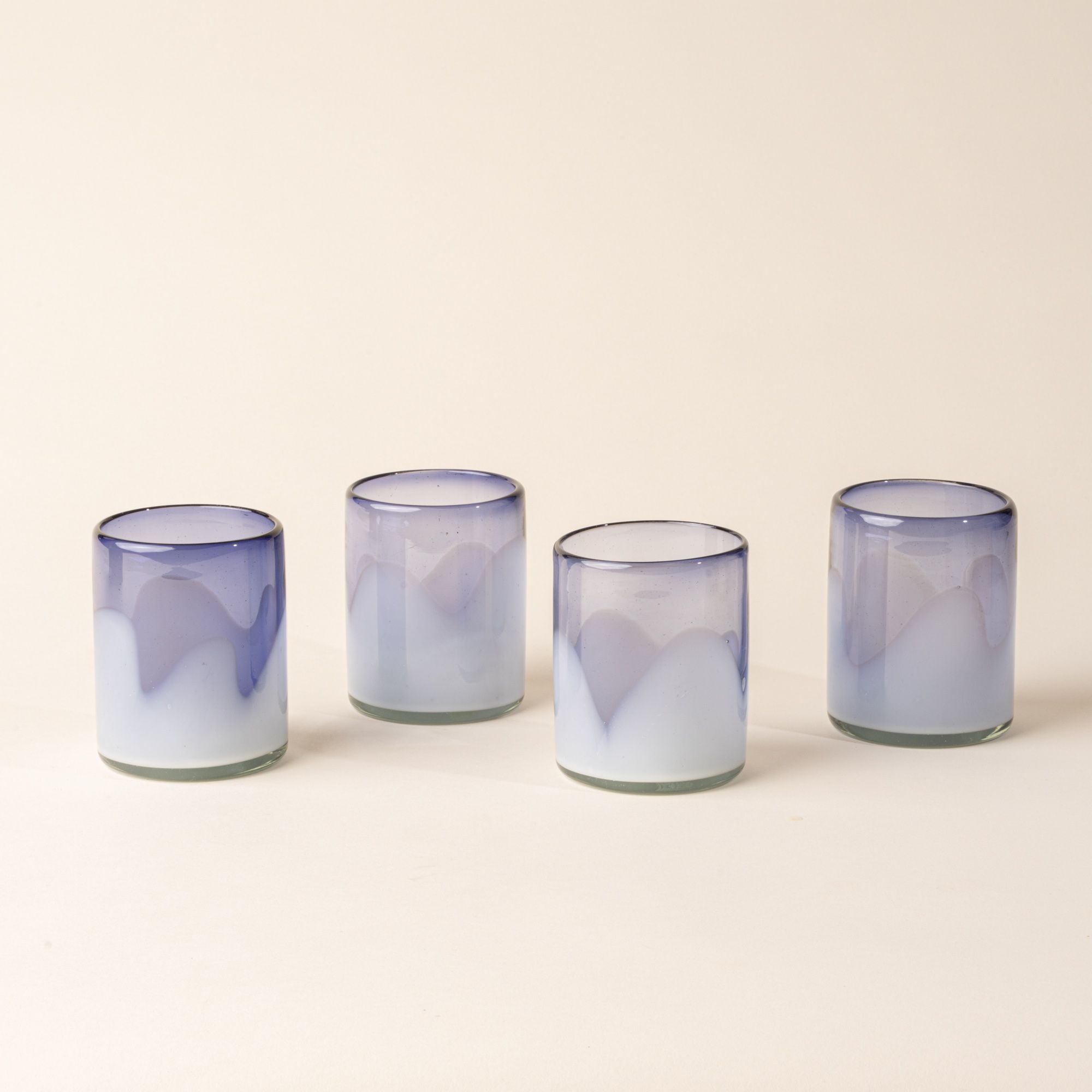Four white and violet handblown glass tumblers with organic wave design, on a beige backdrop.