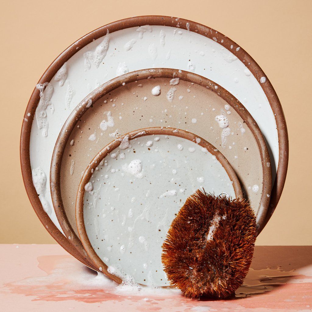 Three plates with soap suds and a palm fiber brush