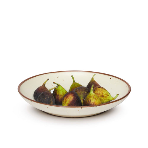 Figs on a large ceramic plate with a curved bowl edge in a warm, tan-toned, off-white color featuring iron speckles and an unglazed rim.