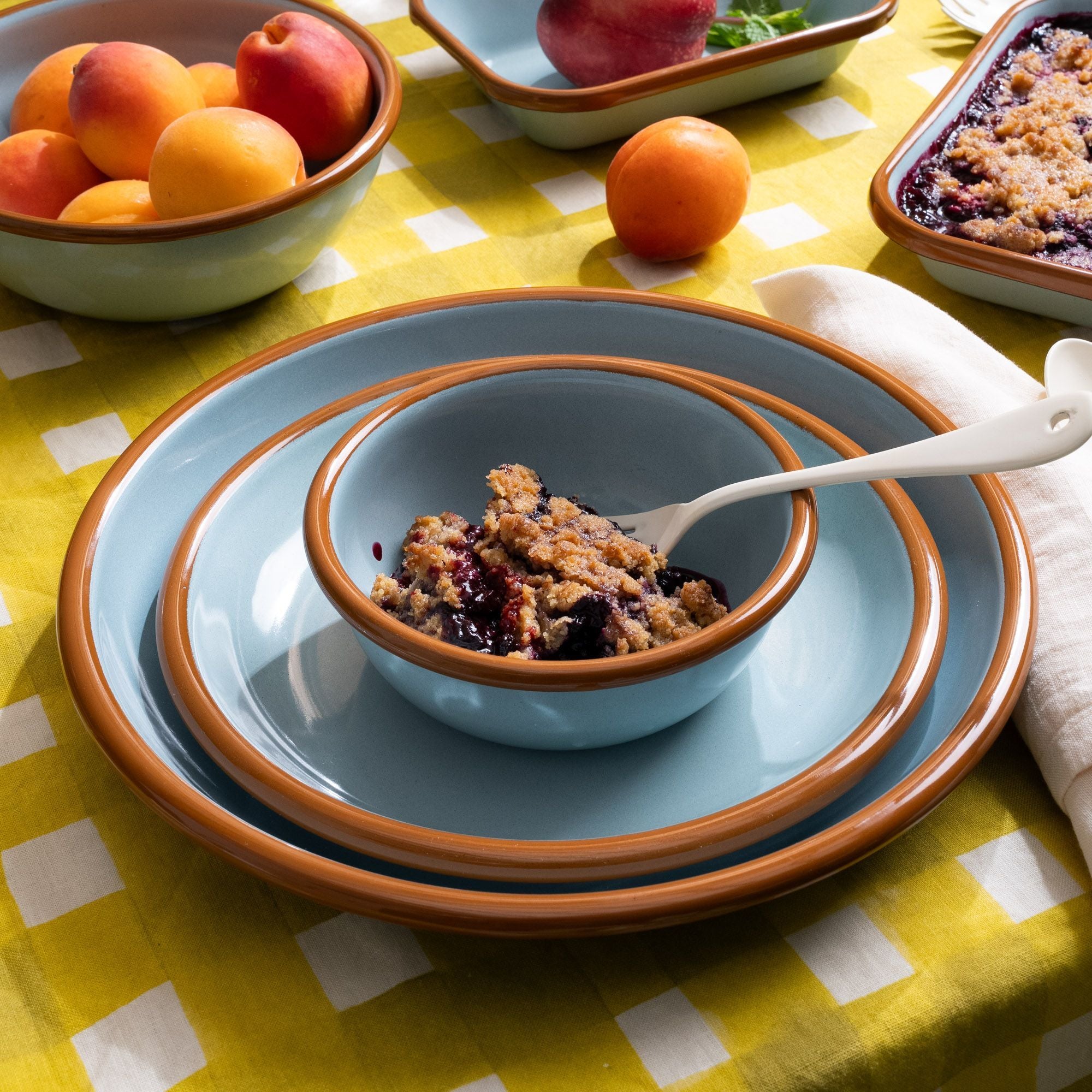 Small bowl with cobbler on a side plate, and dinner plate; all are made of enamel in robin's egg blue with a warm brown rim.