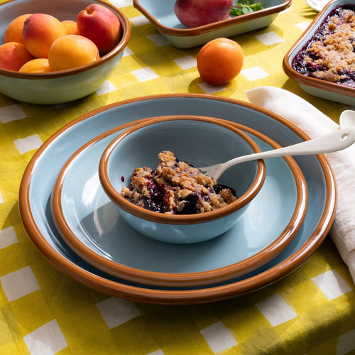 Small bowl with cobbler on a side plate, and dinner plate; all are made of enamel in robin's egg blue with a warm brown rim.