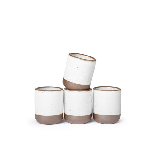 A set of 4 small, short ceramic mug cups in a cool white color featuring iron speckles and unglazed rim and bottom base, stacked in a row of 3, with the 4th on top.