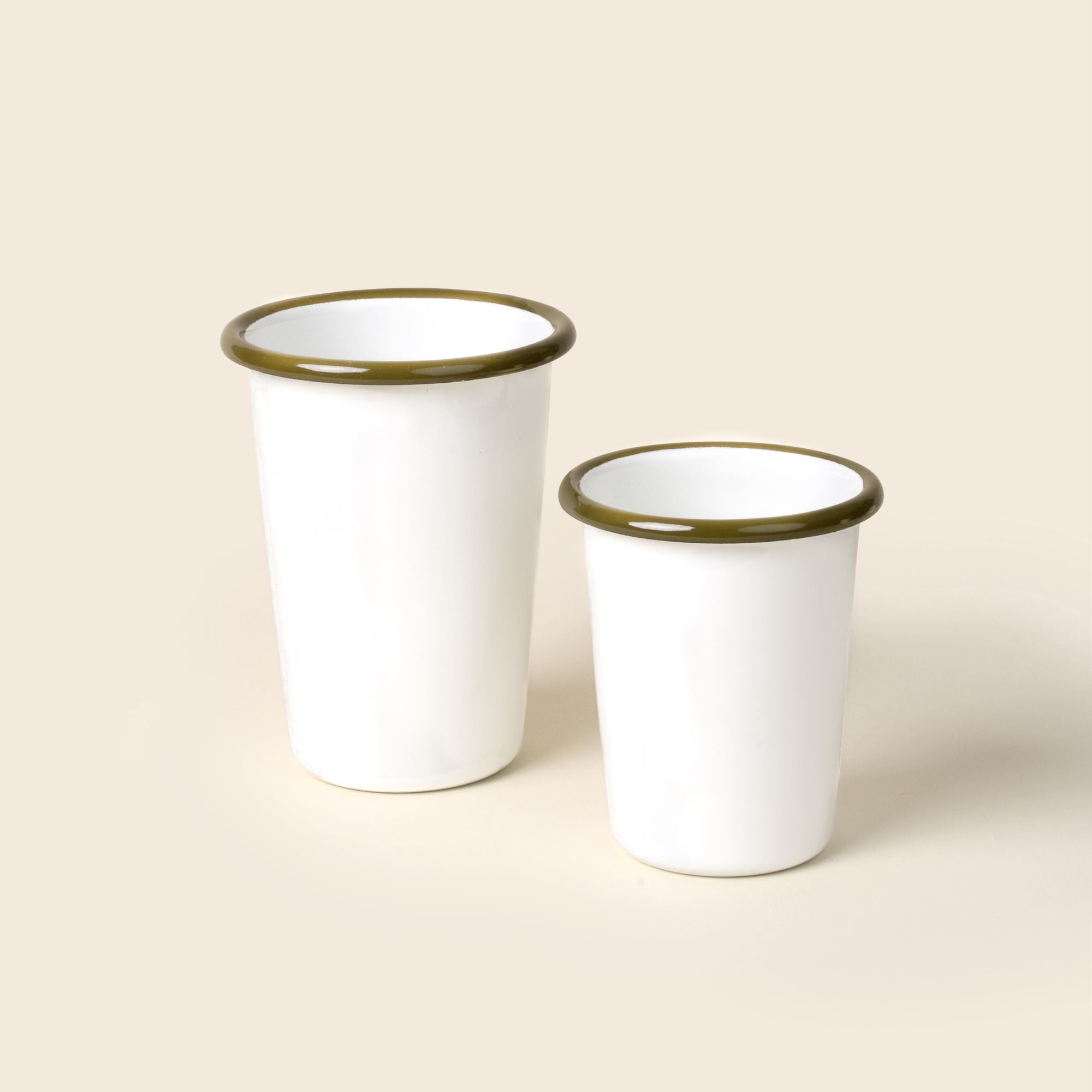 A small and tall white enamel tumblers with an olive green rim, set against a soft beige background.