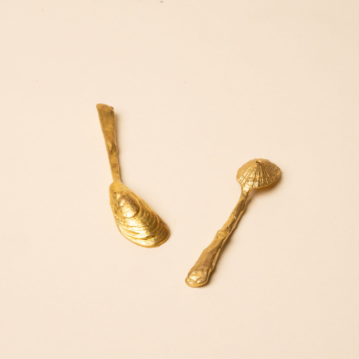 The back of two small handcrafted gold spoons with textured, organic shapes on a neutral background.