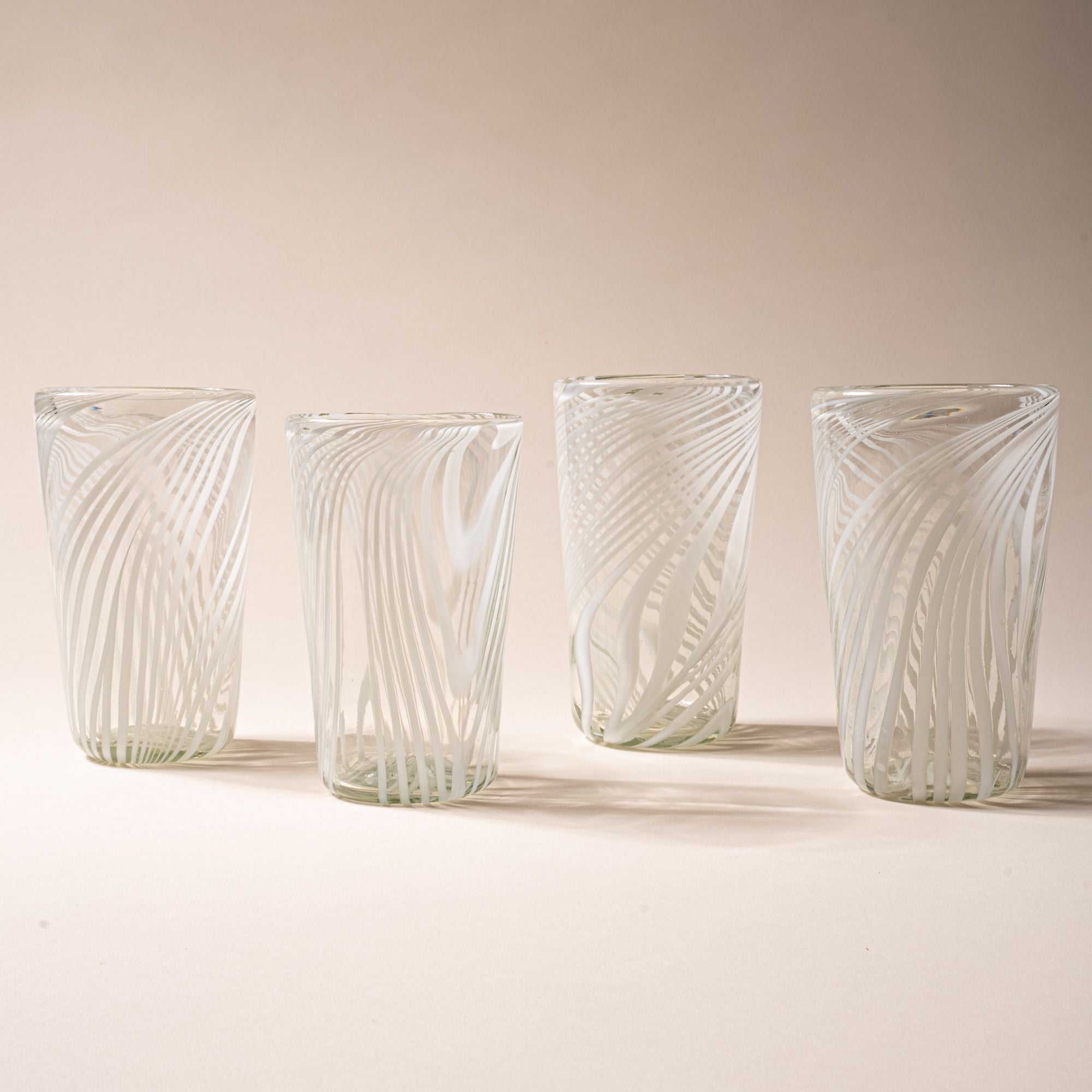 Four clear pint glasses with white diagonal swirl pattern against a neutral background.