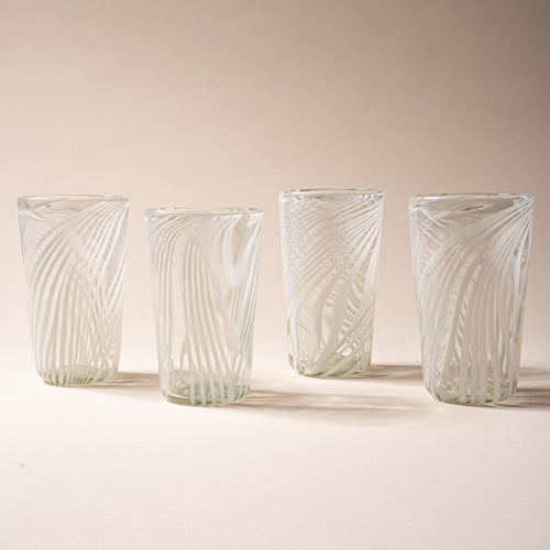 Four clear pint glasses with white diagonal swirl pattern against a neutral background.