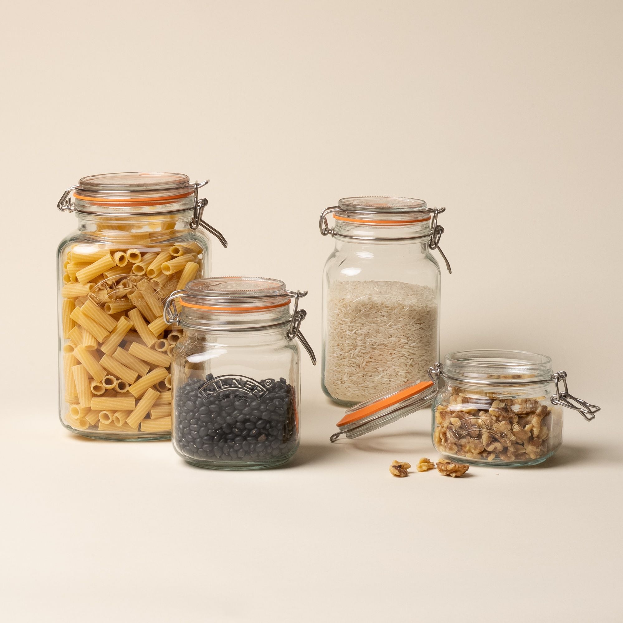 4 storage glass square jars filled with dried goods, in a row of largest to smallest, each topped with a lid with a rubber seal and steel clip closure.