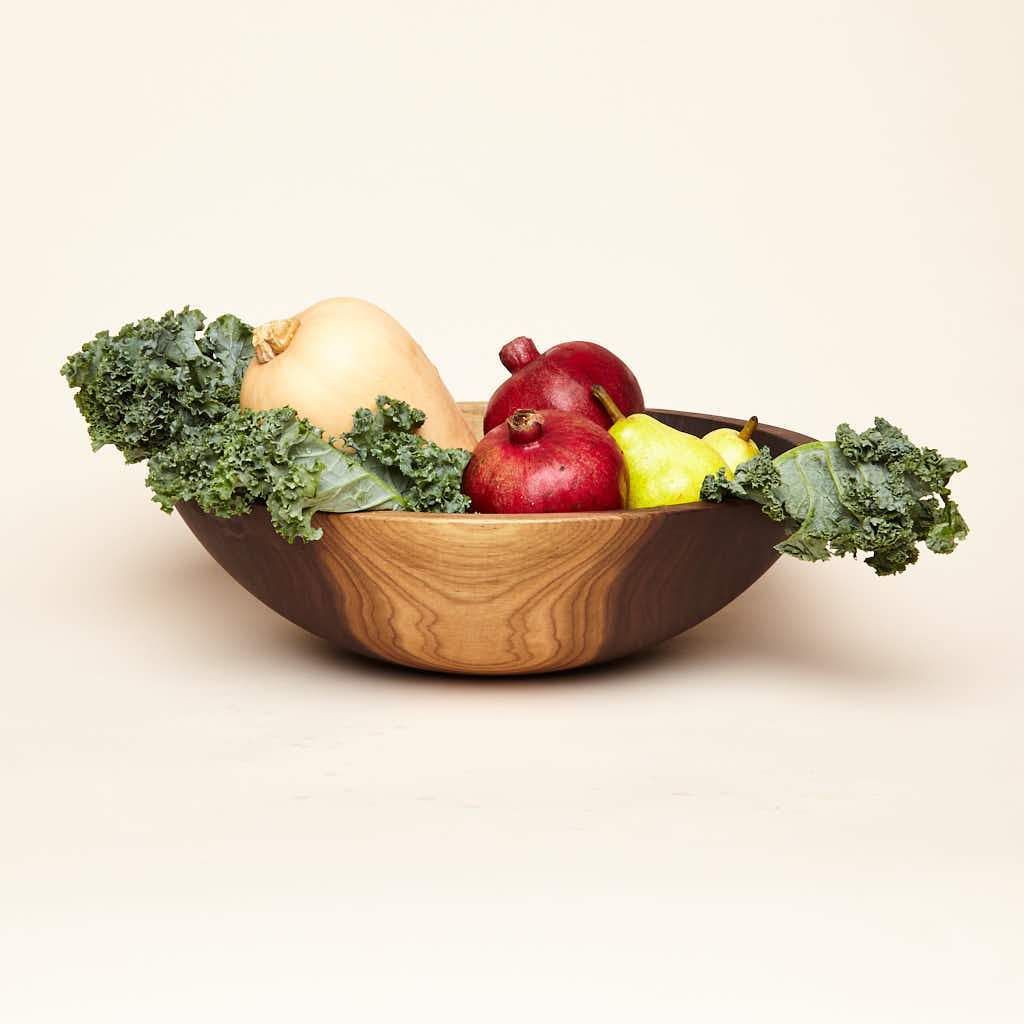 Fruits and vegetables fill a large-sized walnut wood bowl with some maplewood color in the wood
