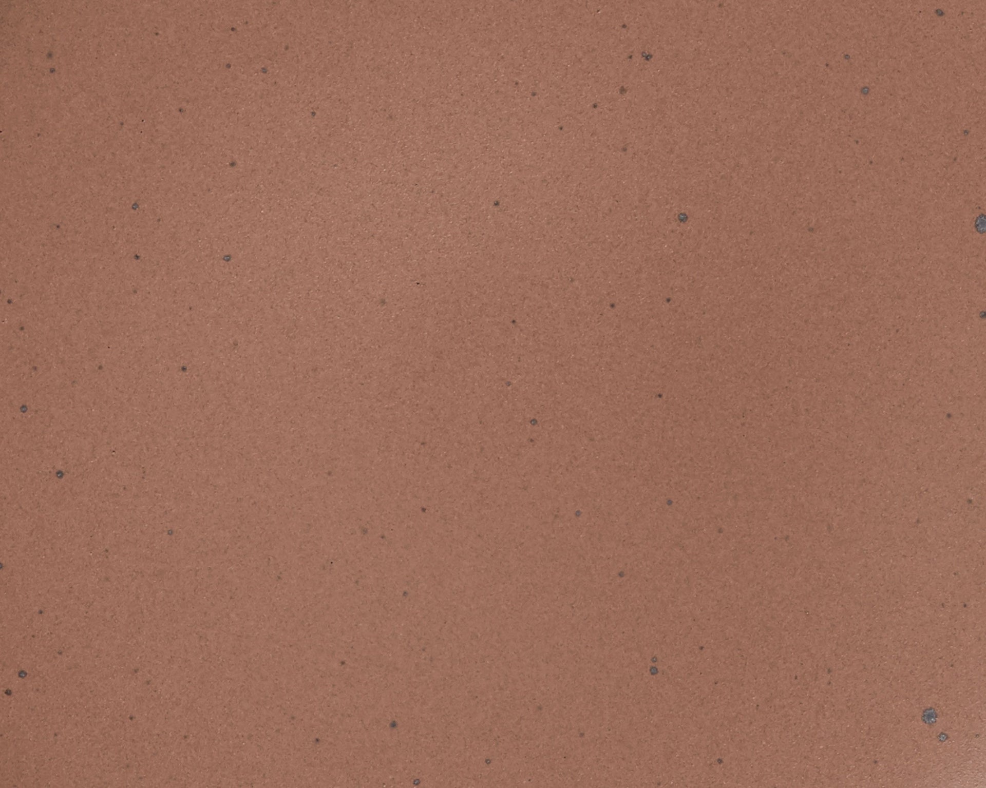 A closeup of a ceramic plate in a warm brown color featuring iron speckles