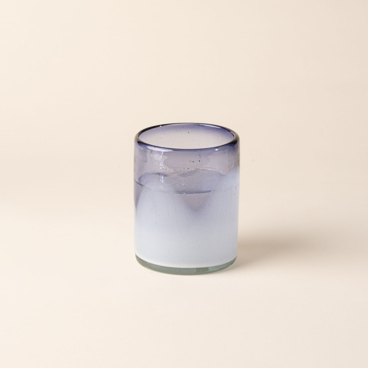 A white and violet handblown glass tumbler with organic wave design, filled with water.