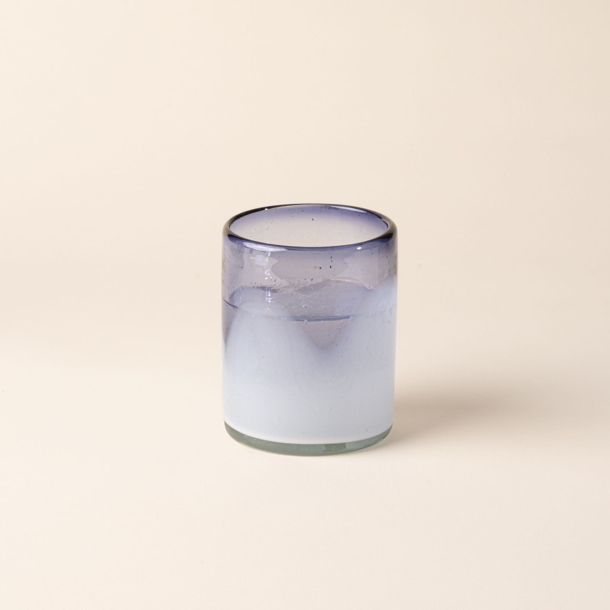 A white and violet handblown glass tumbler with organic wave design, filled with water.