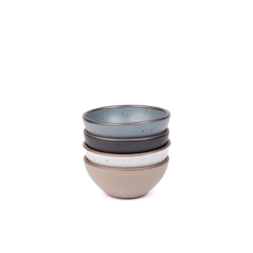 A stack of 4 small dessert sized rounded ceramic bowls in a blue-grey, graphite black, cool white, and warm pale brown colors featuring iron speckles and an unglazed rim