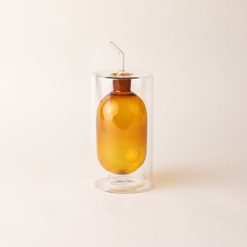 An artful glass cruets in a an orange color. There is a rounded bulb that acts as a container for the cruet, surrounded by a doubled glass wall.