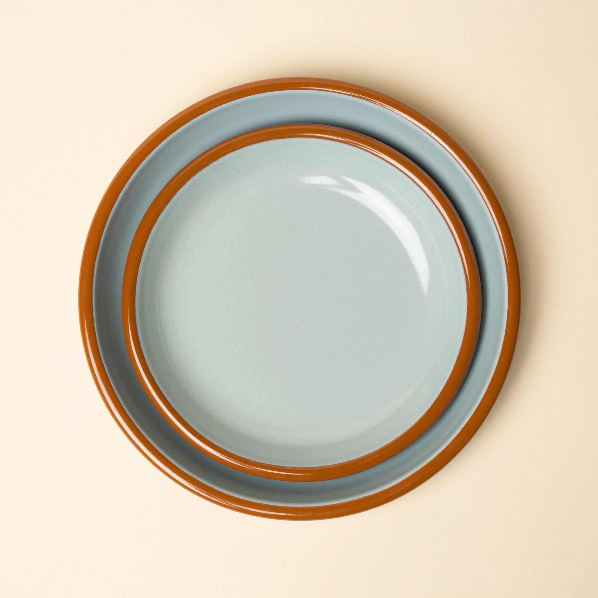 A nesting enamel side plate and dinner plate in robin's egg blue with a warm brown rim.