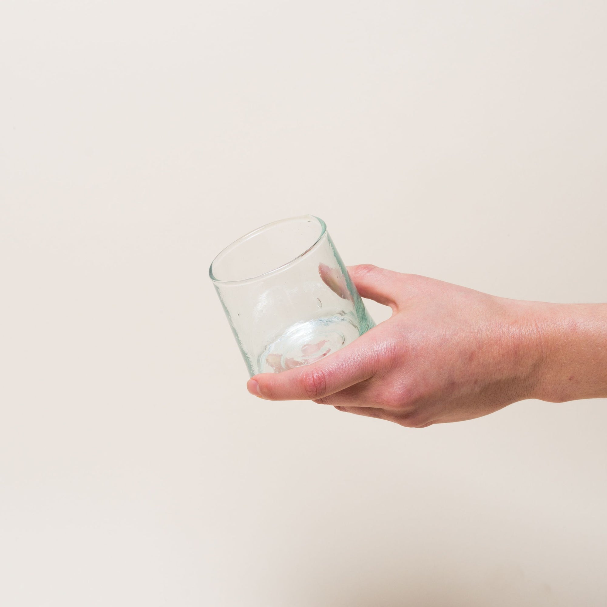 A hand holds a short, empty drinking glass