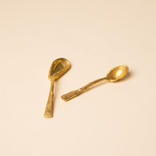 Two small handcrafted gold spoons with textured, organic shapes on a neutral background.