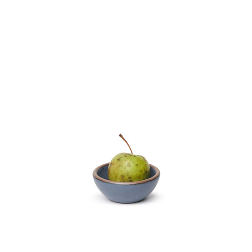 A tiny rounded ceramic bowl in a cool medium blue color featuring iron speckles and an unglazed rim, with a pear inside