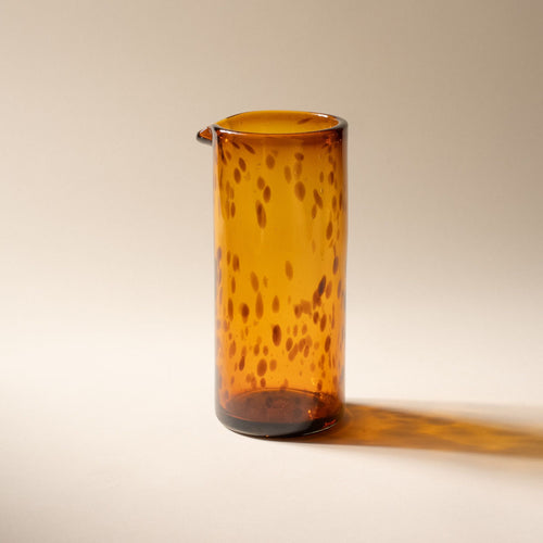 A tortoiseshell tall transparent glass pitcher with small spout at the top