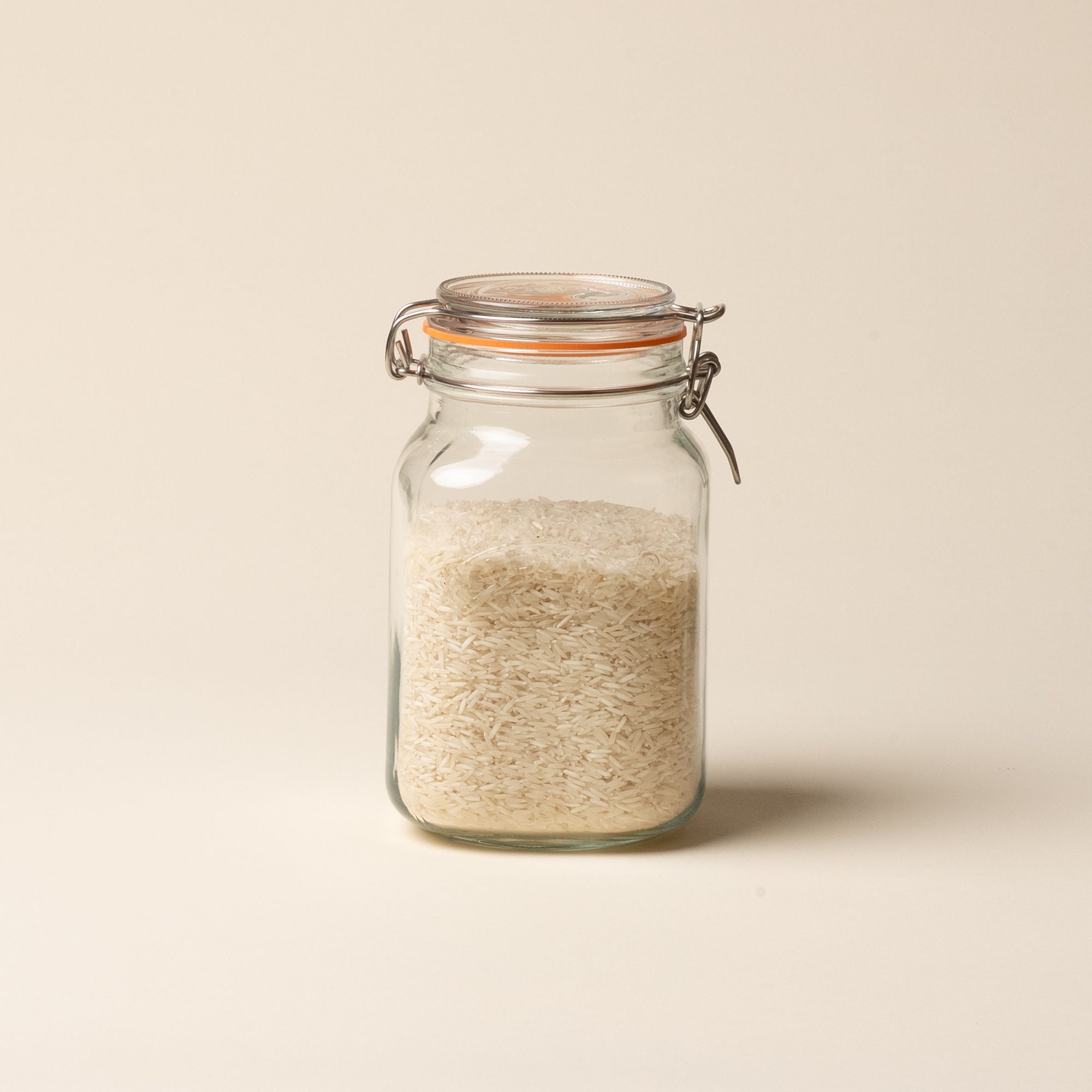 A medium storage glass square jar filled with rice, topped with a lid with a rubber seal and steel clip closure.