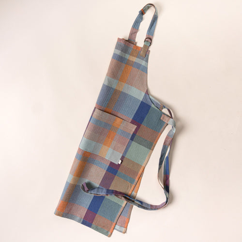 Plaid kitchen apron in muted blue, green, and tan tones with an adjustable neck strap and long waist ties, laid flat on a light background.