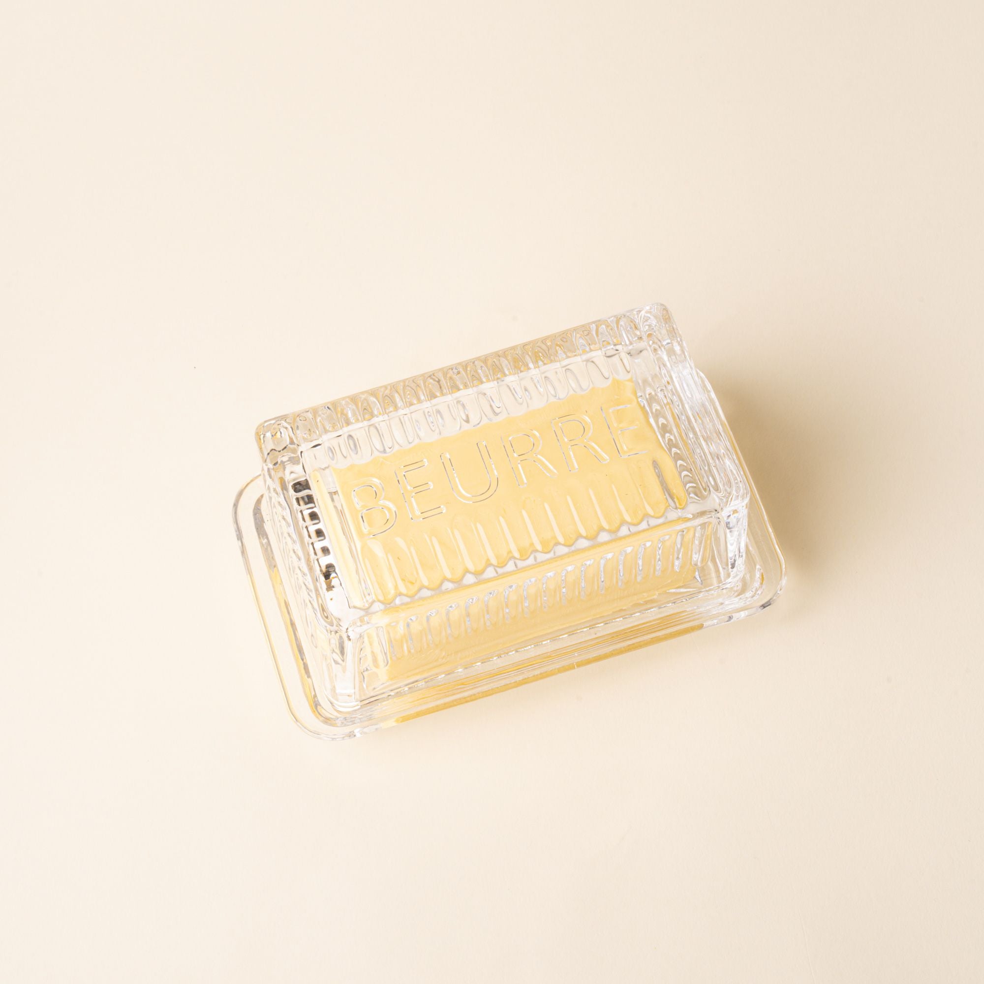 Glass butter dish with lid over butter on a light surface