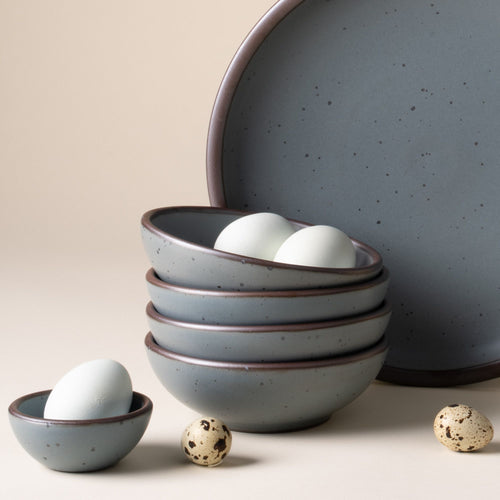 Eggs sits in a stack of 4 small shallow ceramic bowls in a blue-grey color featuring iron speckles and an unglazed rim