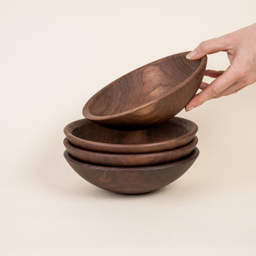 A hand reaches to stack a bowl at the top of a stack of 3 small walnut wood bowls
