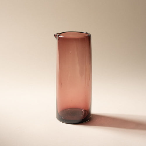 A light plum tall transparent glass pitcher with small spout at the top