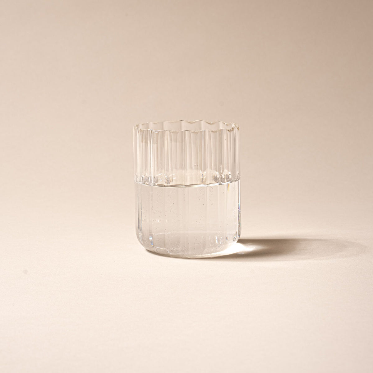 Clear glass of water, half-filled, with vertical ridges on a neutral background.