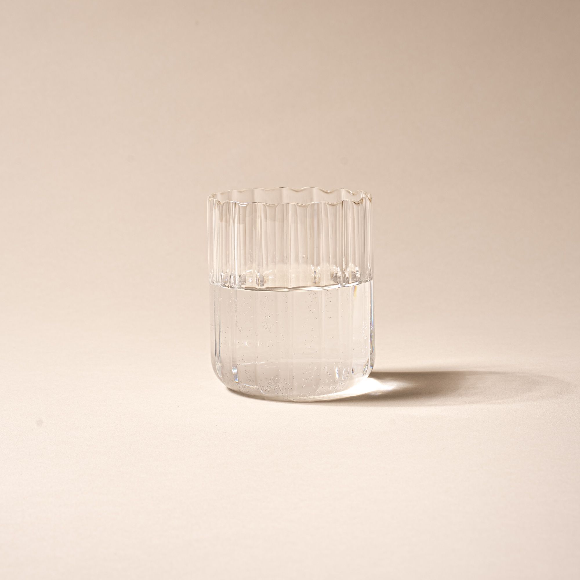 Clear glass of water, half-filled, with vertical ridges on a neutral background.