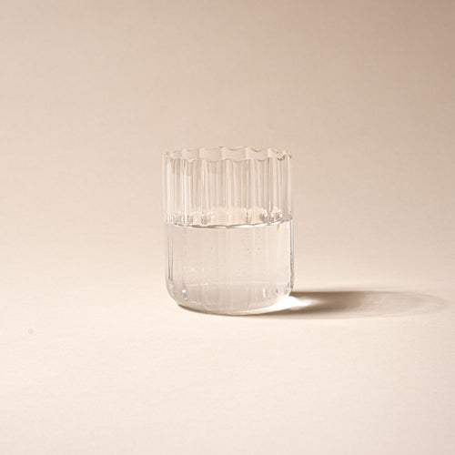 Clear glass of water, half-filled, with vertical ridges on a neutral background.