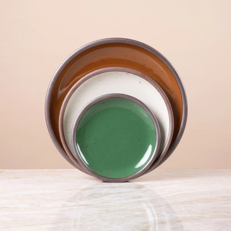 Stacked ceramic plates in glossy green, white, and glossy brown with speckled finish, displayed on a marble surface.