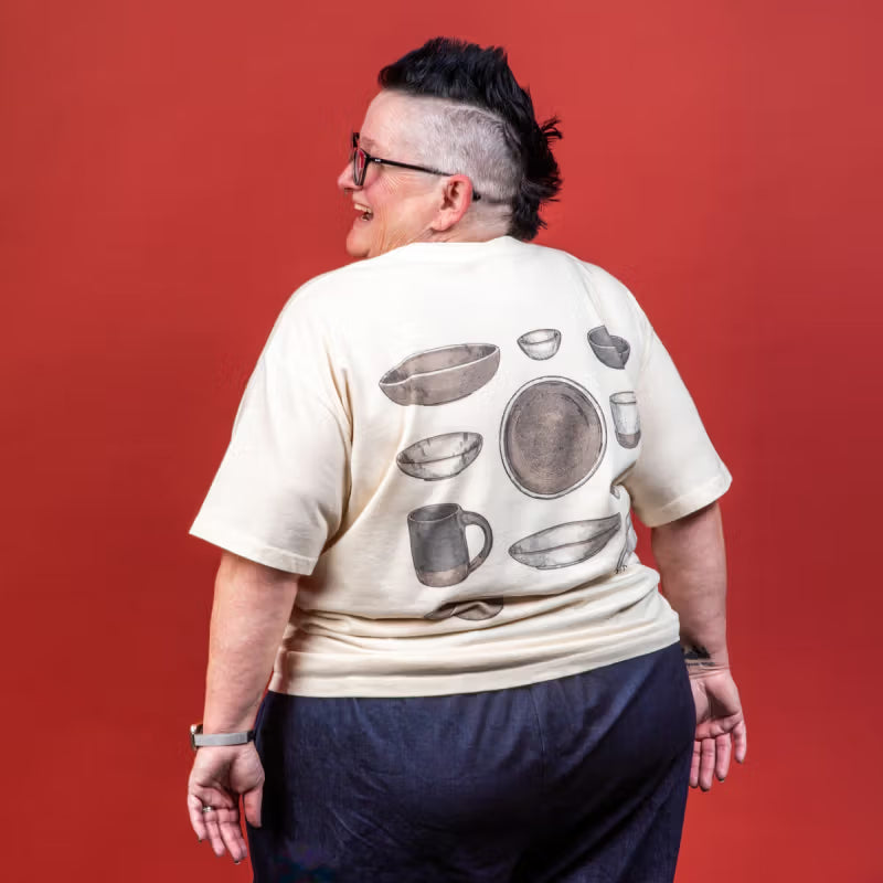 Model wearing the t-shirt from the back and staring off to the side smiling and wearing pink glasses