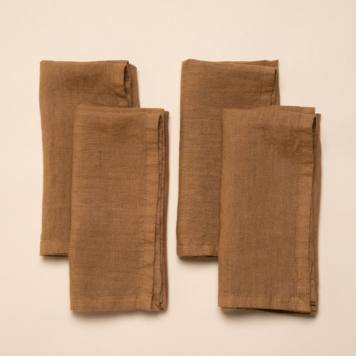 Four neatly folded brown linen napkins arranged in a square on a neutral background.