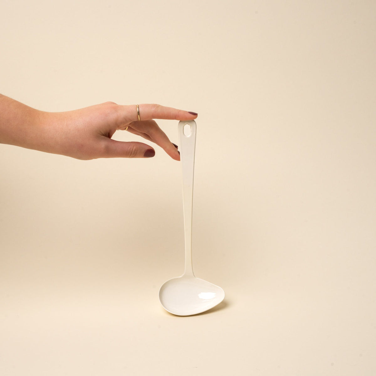 A hand props up a white enamel sauce ladle with a hole at the end of the handle for hanging