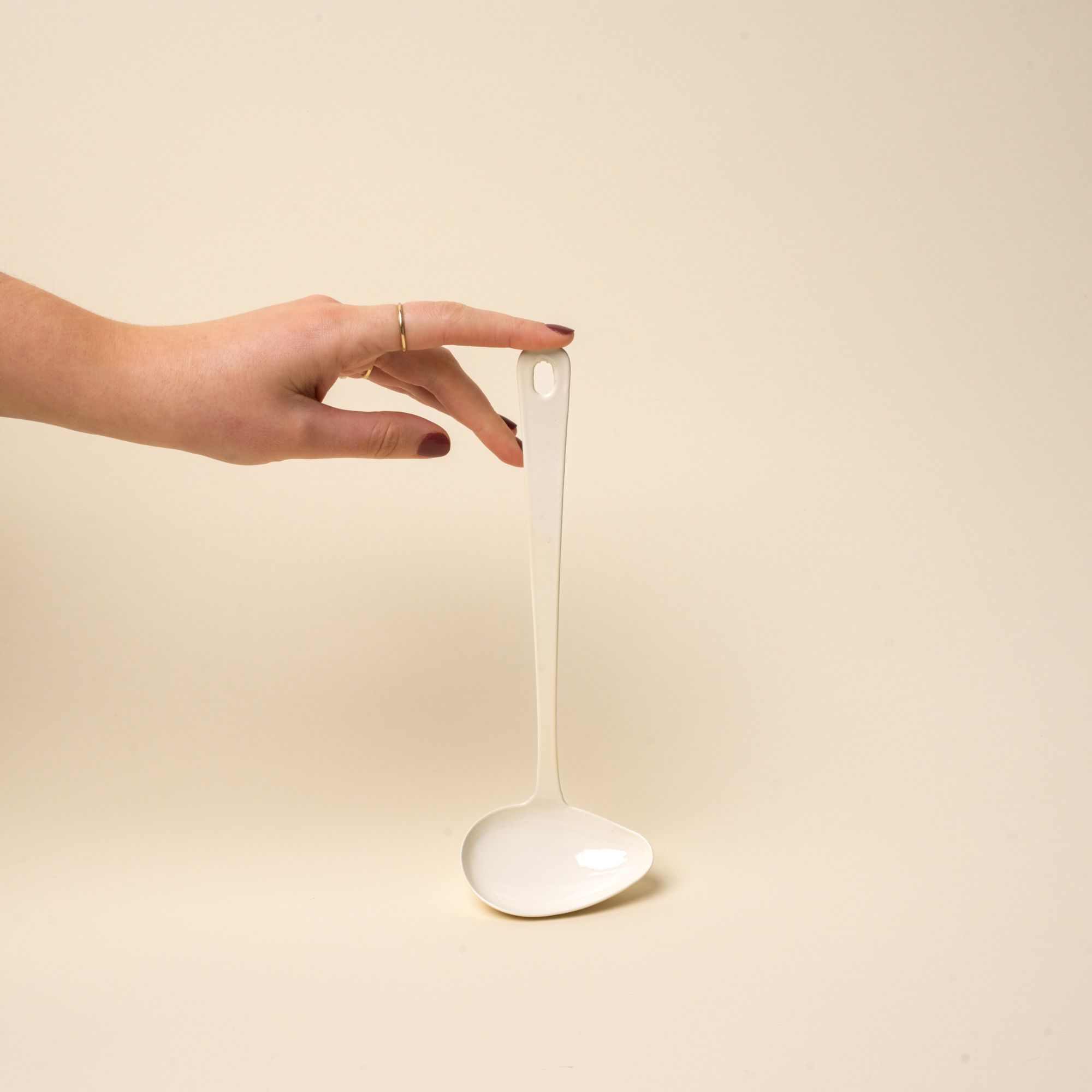 A hand props up a white enamel sauce ladle with a hole at the end of the handle for hanging