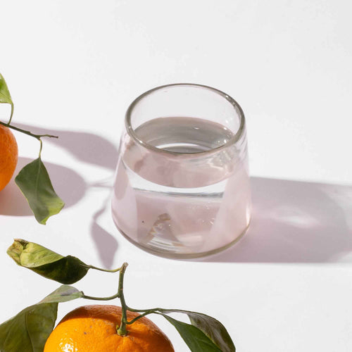 A short clear glass with pale light pink arch base filled with water next to clementines