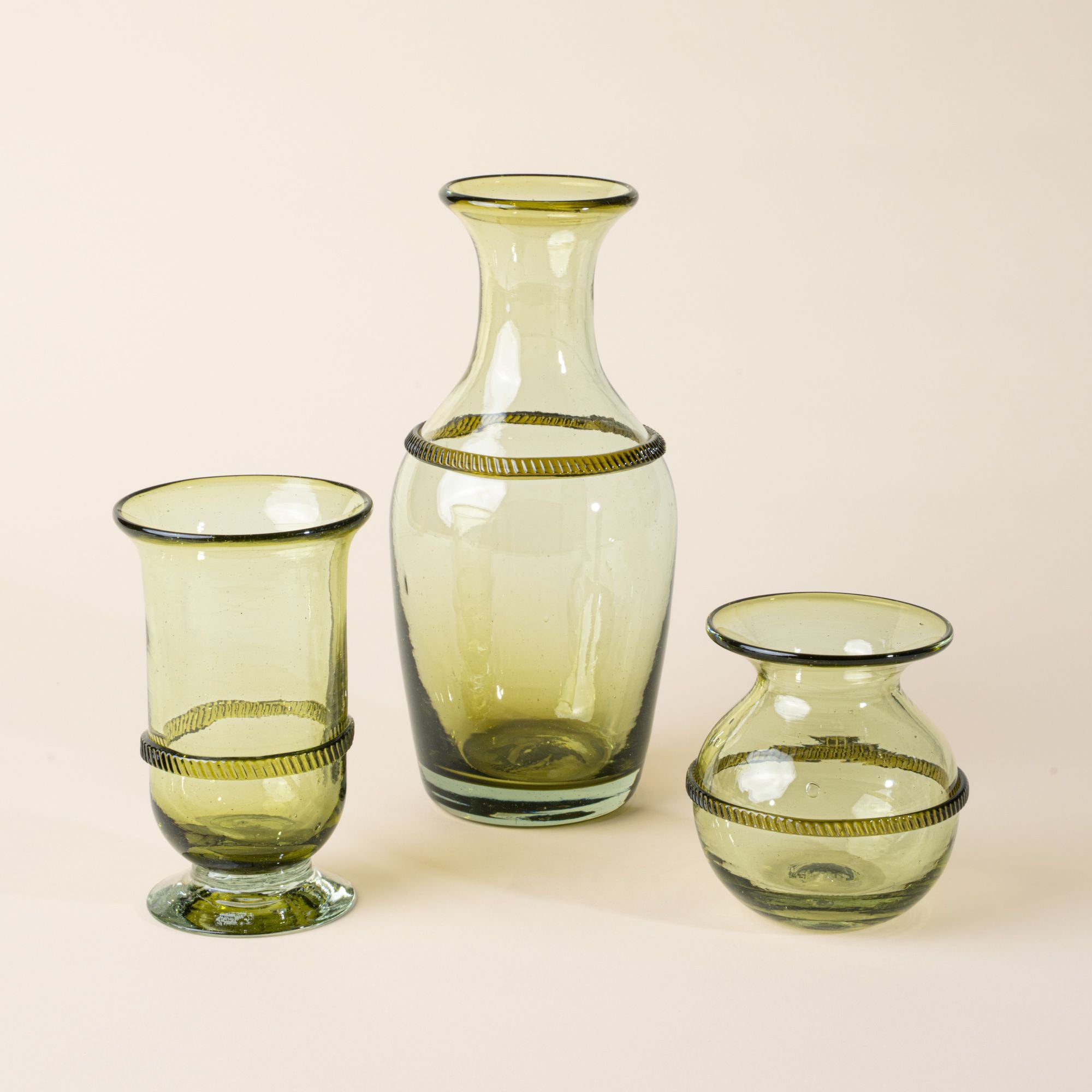 Set of three light green glass vessels—a tall flared vase, a pedestal vase, and a small rounded vase—each with a decorative band around the center, displayed against a neutral background.