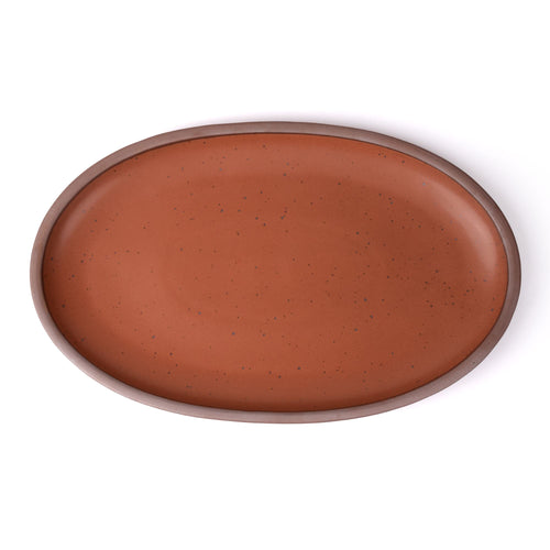 A large oval ceramic platter in a cool terracotta featuring iron speckles and an unglazed rim