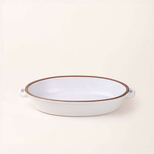 A large, oval, matte, cool white ceramic baking dish with two side handles, on a solid off-white background.