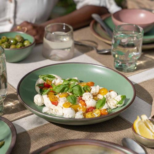 A shallow ceramic bowl-plate with a wide rim for composed dishes in a viridian green glaze with a matte finish.