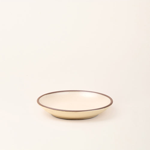A medium ceramic plate with a curved bowl edge in a cream color featuring iron speckles and an unglazed rim.