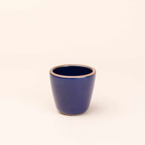 A short cup that tapers out to get wider at the top in a glossy dark blue color featuring iron speckles